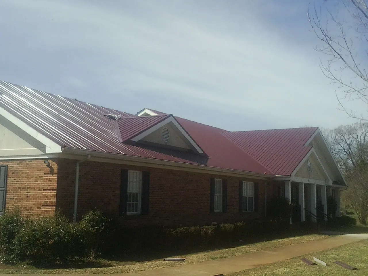 Red metal roof with gabled entries on a long brick building, from a Hail Damage Roof Repair job in Bovill