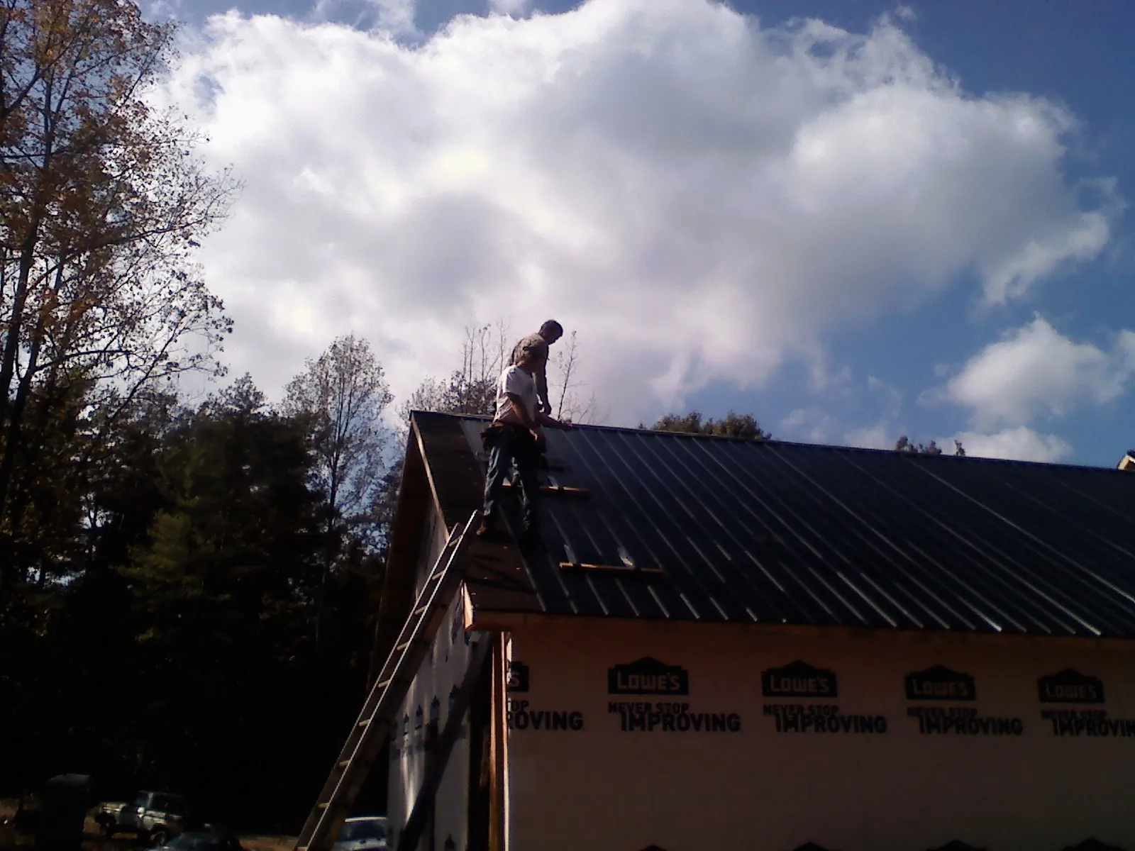 Roofer fastening dark metal panels high against a cloudy sky, from a Roof Inspection job in Bovill