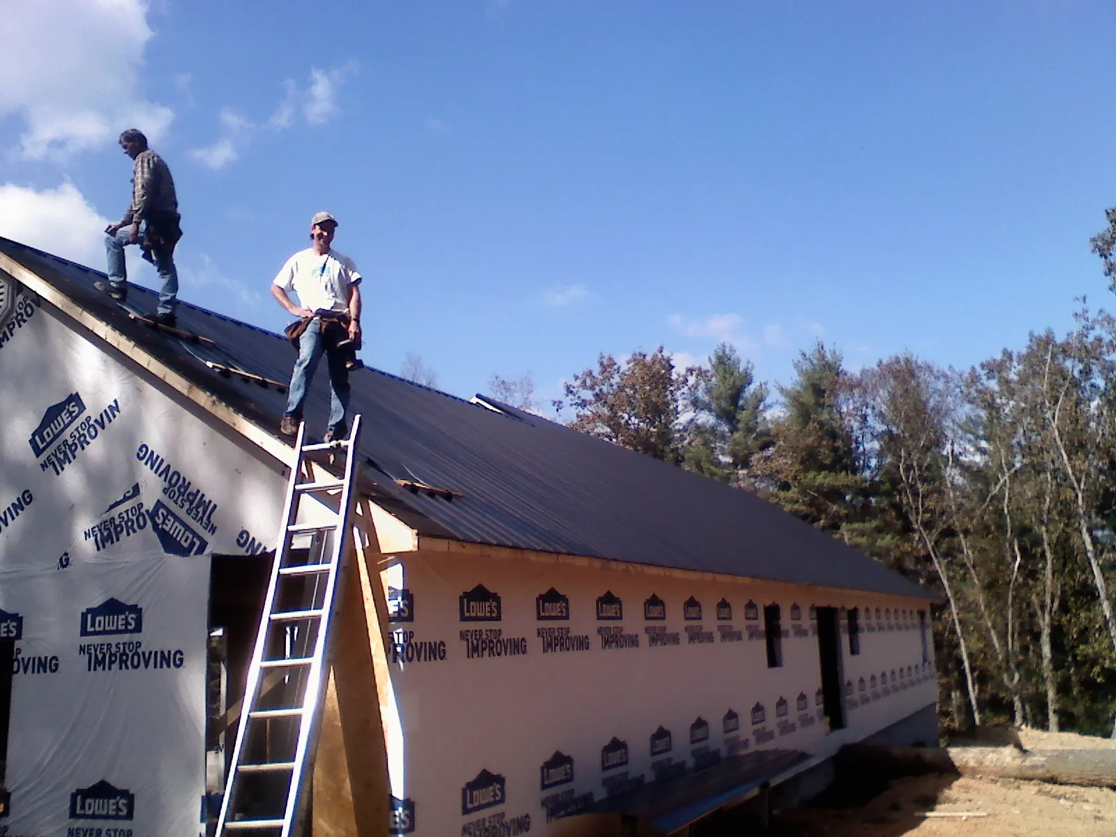 Two roofers standing on a long dark metal roof over a wrapped building in Bovill